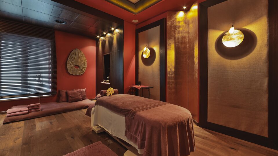 A stylish spa room with a massage table and soft lighting. The walls are painted in warm tones, creating a relaxing atmosphere.