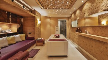 An elegant spa room with soothing colors and a relaxing ambiance. There is a massage table and comfortable seating.