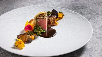 An artfully arranged plate with meat and colorful sides. The presentation includes edible flowers and various textures.