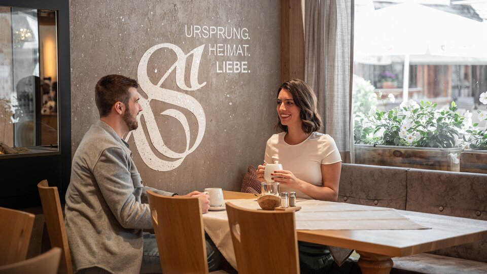 A cozy café with a couple talking to each other. On the wall is the inscription "ORIGIN HOME LOVE".