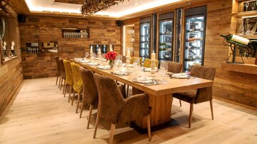 An elegant dining room with a long wooden table and upholstered chairs. The walls are made of wood, and the room has a cozy atmosphere.