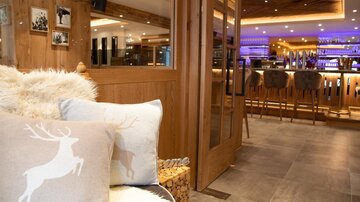 A modern restaurant with warm wood design and stylish bar stools. Cozy cushions with a deer motif are lying on the sofa.