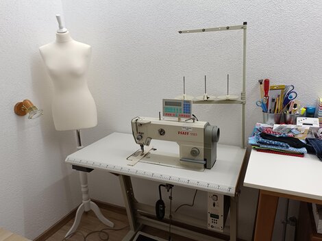 A bright sewing room with a sewing machine and a dress form. Various sewing tools and fabrics are visible on the table.