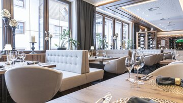 An elegant restaurant with bright window fronts and modern furniture. The table is lovingly set, and the room feels welcoming.