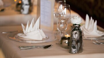 An elegantly set table with folded napkins and glasses. In the center is a stylish vase with a flower and a candle.