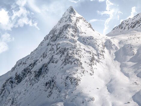 A majestic mountain with snow-covered slopes under a cloudy sky. The peaks are bathed in radiant sunlight.