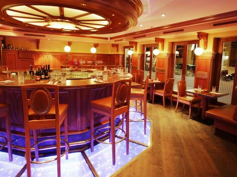 A stylish bar with wooden paneling and a illuminated counter. Cozy seating completes the inviting atmosphere.
