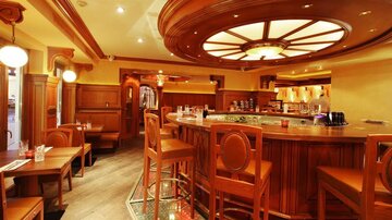An elegant bar with wooden interiors and an inviting atmosphere. High chairs and tables invite you to linger.