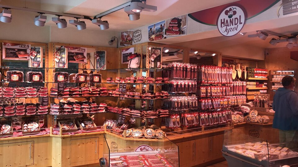 A butcher shop with many meat products and wooden shelves. The walls are decorated with various types of sausage.