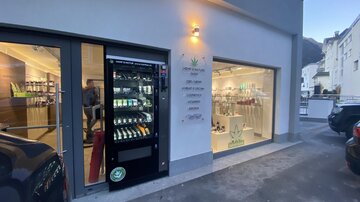 A modern vending machine next to a store entrance. The store is brightly lit and offers a wide selection of products in the window.