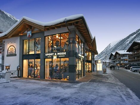 A modern shop in the Alps, surrounded by snow-capped mountains. The facade is extensively glazed and inviting.