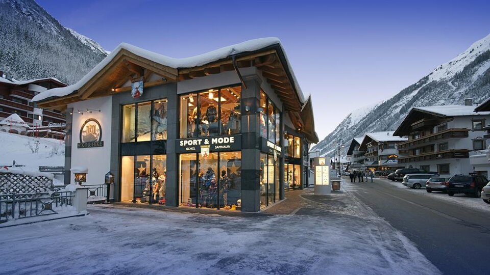 A modern shop in the Alps, surrounded by snow-capped mountains. The facade is extensively glazed and inviting.