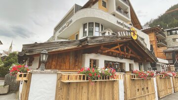 A charming hotel with a wooden-clad facade and colorful flowers. In the background, traditional alpine buildings are visible.