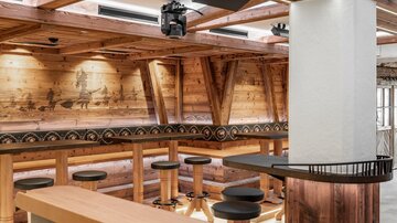 A cozy interior with wooden walls and a modern bar. There are high seating areas and pleasant lighting.
