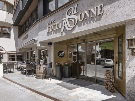 Der Eingang zum Hotel Sonne ist stilvoll gestaltet und einladend. Es gibt Sitzgelegenheiten im Freien und eine moderne Fassade.