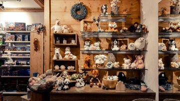 A cozy shop with shelves full of plush toys. On a large table, more stuffed animals and decorations are placed.