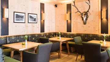 A cozy restaurant with wooden walls and modern furniture. A deer antler hangs on the wall, and the tables are decorated with fresh flowers.
