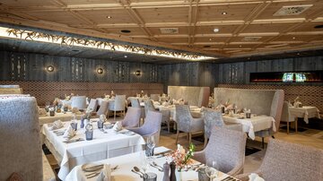 An elegant restaurant with stylish tables and cozy seating. The beautiful wooden ceiling and decorative lighting create an inviting atmosphere.