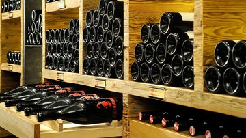 A shelving system with many wine bottles in dark and light wooden crates. The bottles are neatly stacked and waiting for sale.