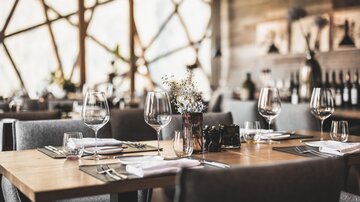 Ein elegantes Restaurant mit Holztischen und stilvollen Stühlen. Die Tische sind liebevoll mit Glaswaren und Blumen dekoriert.