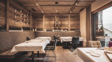 Ein modernes Restaurant mit Holzwänden und eleganten Tischen. Die Atmosphäre ist gemütlich und einladend mit großen Fenstern, die Licht hereinlassen.