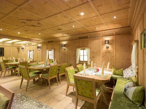 A cozy room with wooden walls and elegant furnishings. Several tables and chairs are ready for guests.