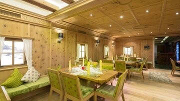 A cozy restaurant with wooden decor and green accents. The tables are decorated for guests and invite them to linger.