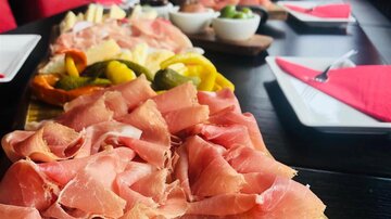 A wooden plate with thinly sliced ham and colorful vegetables. In the background, other plates and an inviting table decoration can be seen.