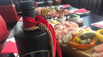 An elegantly set table with a selection of meat platters and sides. In the foreground is a bottle of Kiwi Gin with a red ribbon.
