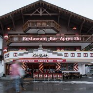 Ein gemütliches Restaurant mit einer Bar im Après-Ski-Stil. Die Fassade ist rustikal mit Holzdetails und einem einladenden Außenbereich.