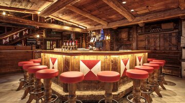 A cozy bar with a round wooden counter and red bar stools. The atmosphere is rustic and inviting.
