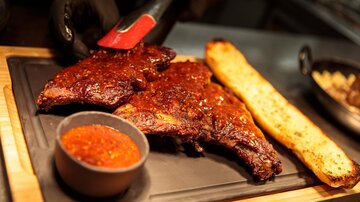 A delicious BBQ rib on a black board. Next to the rib is a dip and a piece of crispy bread.