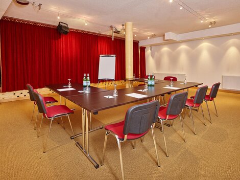 A modernly equipped meeting room with a large table and red chairs. The walls are decorated with red curtains and soft lighting.