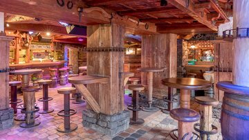A cozy bar with wooden paneling and several high tables. The decor conveys a rustic atmosphere.