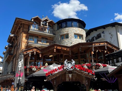 A cozy restaurant with a wooden façade and terraces. Flowers and decorations give the view an inviting charm.
