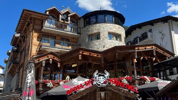 A cozy restaurant with a wooden façade and terraces. Flowers and decorations give the view an inviting charm.