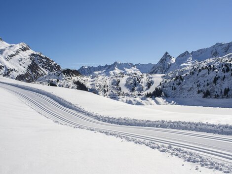 A snowy mountain landscape under a clear blue sky. Ski tracks lead through the untouched snow cover.
