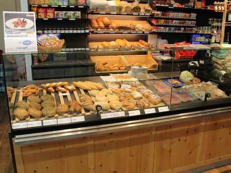 Eine Bäckerei mit einer Auswahl an Gebäck und Brötchen. Im Hintergrund sind verschiedene Snacks und Getränke zu sehen.