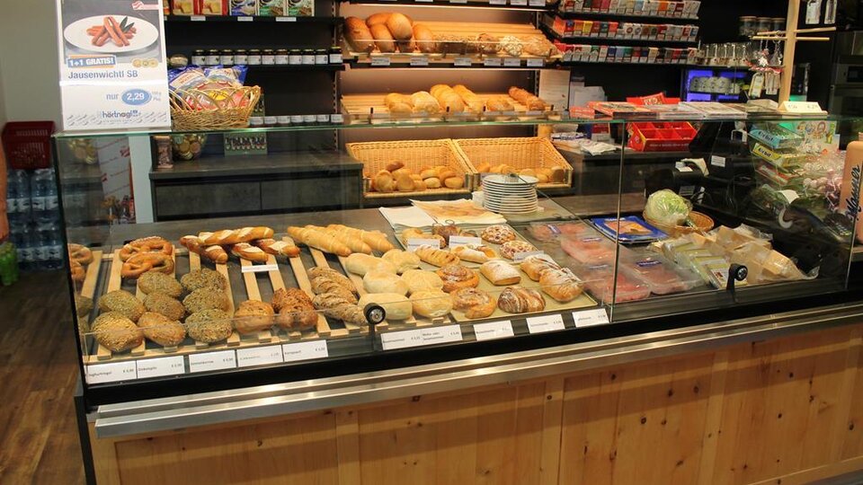 Eine Bäckerei mit einer Auswahl an Gebäck und Brötchen. Im Hintergrund sind verschiedene Snacks und Getränke zu sehen.