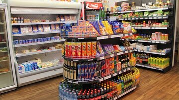 Ein gut sortierter Lebensmittelladen mit Regalen voller Snacks, Getränken und Konserven. Auf der linken Seite befindet sich eine Kühltruhe mit verschiedenen Milchprodukten.
