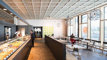 Ein modernes Restaurant mit einer luftigen Atmosphäre. An der Theke sind verschiedene Speisen und Getränke erhältlich, während Gäste an Tischgruppen sitzen. | © MPREIS Warenvertriebs GmbH