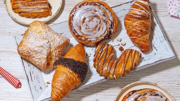 Eine verlockende Auswahl an Gebäck auf einem weißen Holzbrett. Es sind verschiedene Teilchen wie Croissants, Zimtschnecken und gefüllte Teigwaren zu sehen. | © MPREIS Warenvertriebs GmbH