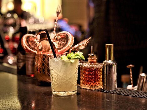 A delicious cocktail with fresh mint is on an elegant bar. In the background, various bottles and utensils are visible.