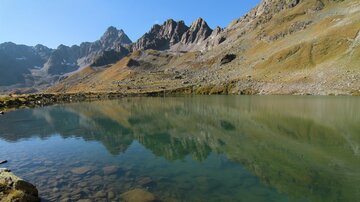 Ein ruhiger See, umgeben von beeindruckenden Bergen. Das klare Wasser spiegelt die Landschaft wider.