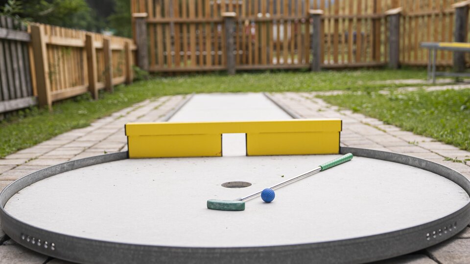 Ein Minigolfplatz mit einer runden Spielfläche und einer gelben Zielwand. Der Ball und der Schläger sind bereit zum Spielen.