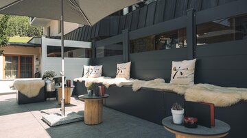 Eine stilvolle Lounge-Ecke im Freien mit gemütlichen Sitzpolstern und Sonnenschirm. Der Raum ist modern gestaltet und bietet eine entspannte Atmosphäre.