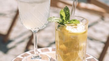 Zwei erfrischende Cocktails auf einem Tisch. Der eine ist klar mit Sahne und der andere ist gelb und mit Minze garniert.