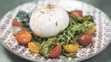 Ein Teller mit frischem Gemüse und einem perfekten Burrata. Rote und gelbe Tomaten sowie Rucola sind schön angerichtet.