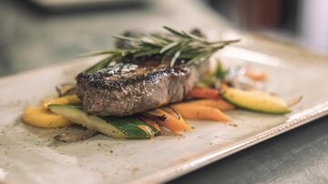 Ein saftiges Stück Fleisch auf einem Bett aus buntem Gemüse. Das Gericht ist mit frischen Kräutern garniert.