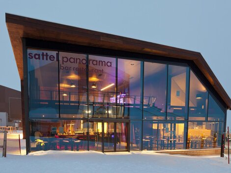 A modern restaurant with large glass windows and a simple wood design. The building is located in a winter setting with snow.